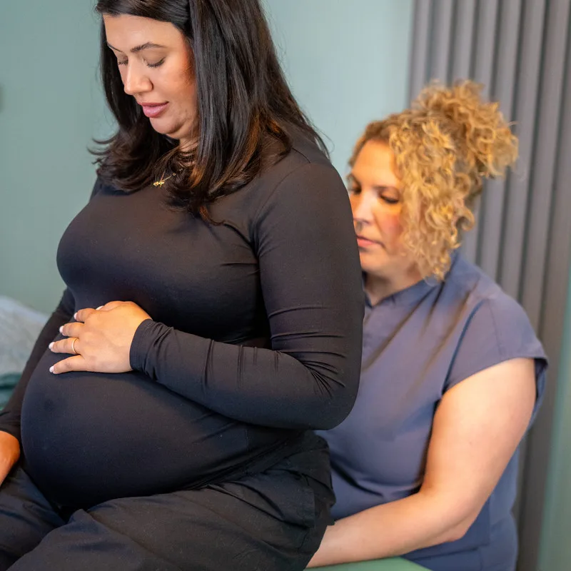 An osteopath supporting a pregnant patient sitting on the treatment couch