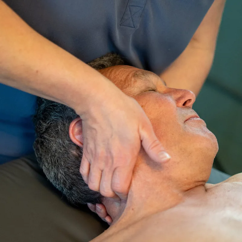 An osteopath treating an adult patient's neck on the couch