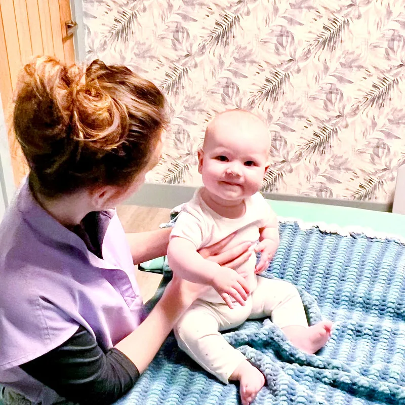 An osteopath sitting with a baby on the treatment table at the clinic
